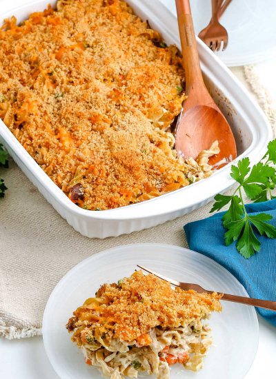 The finished Tuna Noodle Casserole with some on a white plate and the whole casserole behind it.