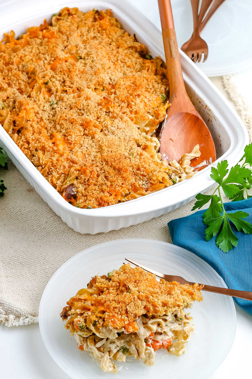 The finished Tuna Noodle Casserole with some on a white plate and the whole casserole behind it. 