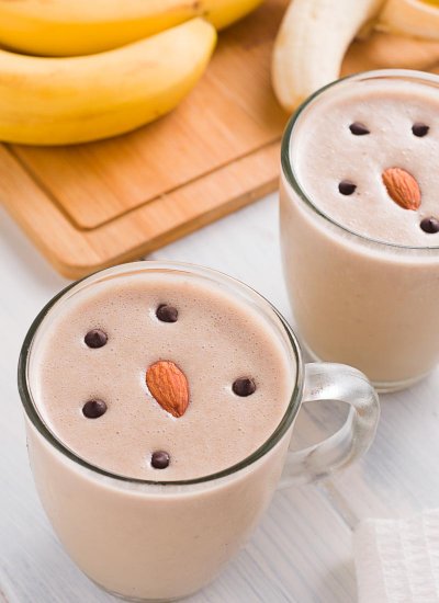 A Peanut Butter Banana Smoothie in a clear glass cup with a banana in the background.