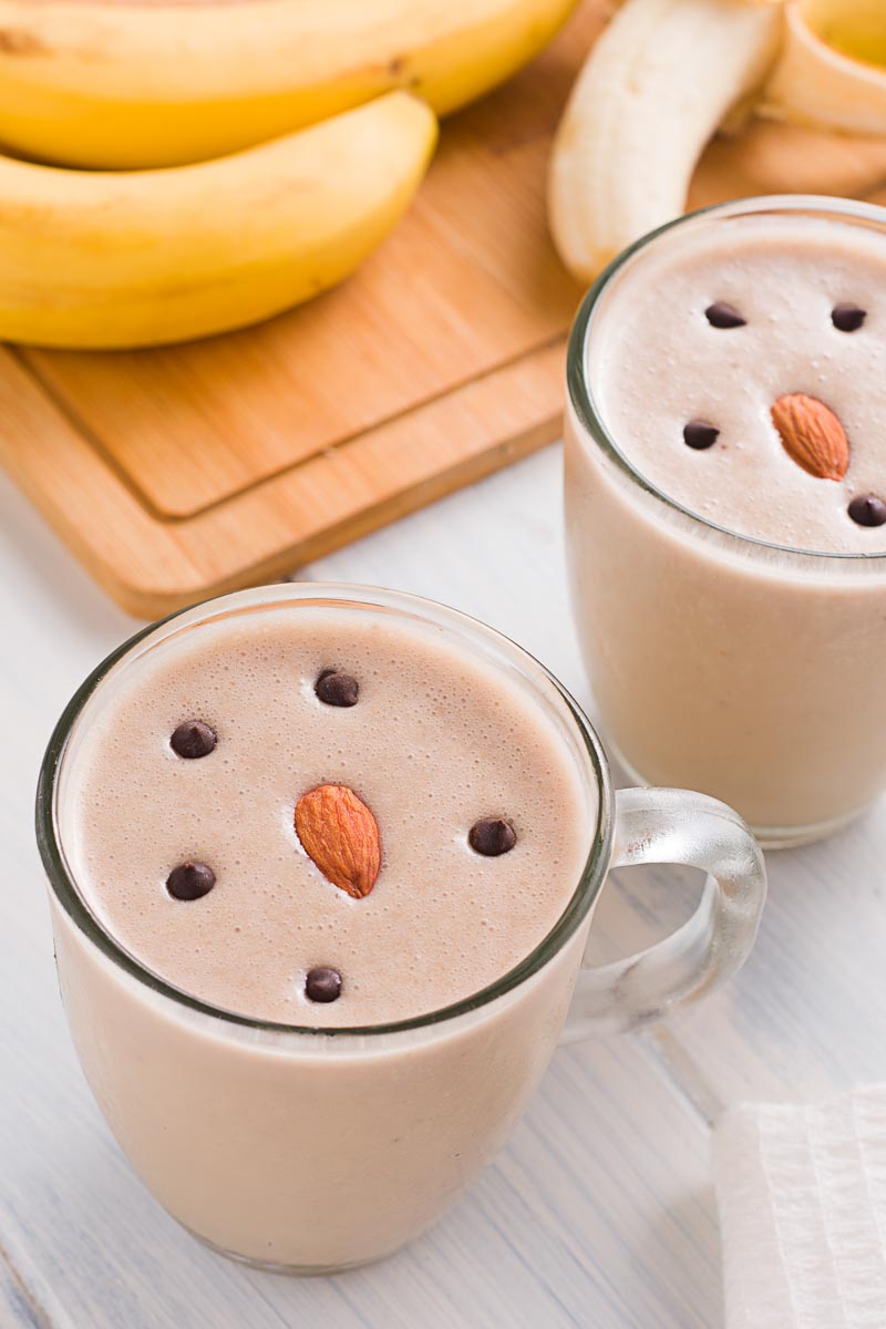 A Peanut Butter Banana Smoothie in a clear glass cup with a banana in the background. 
