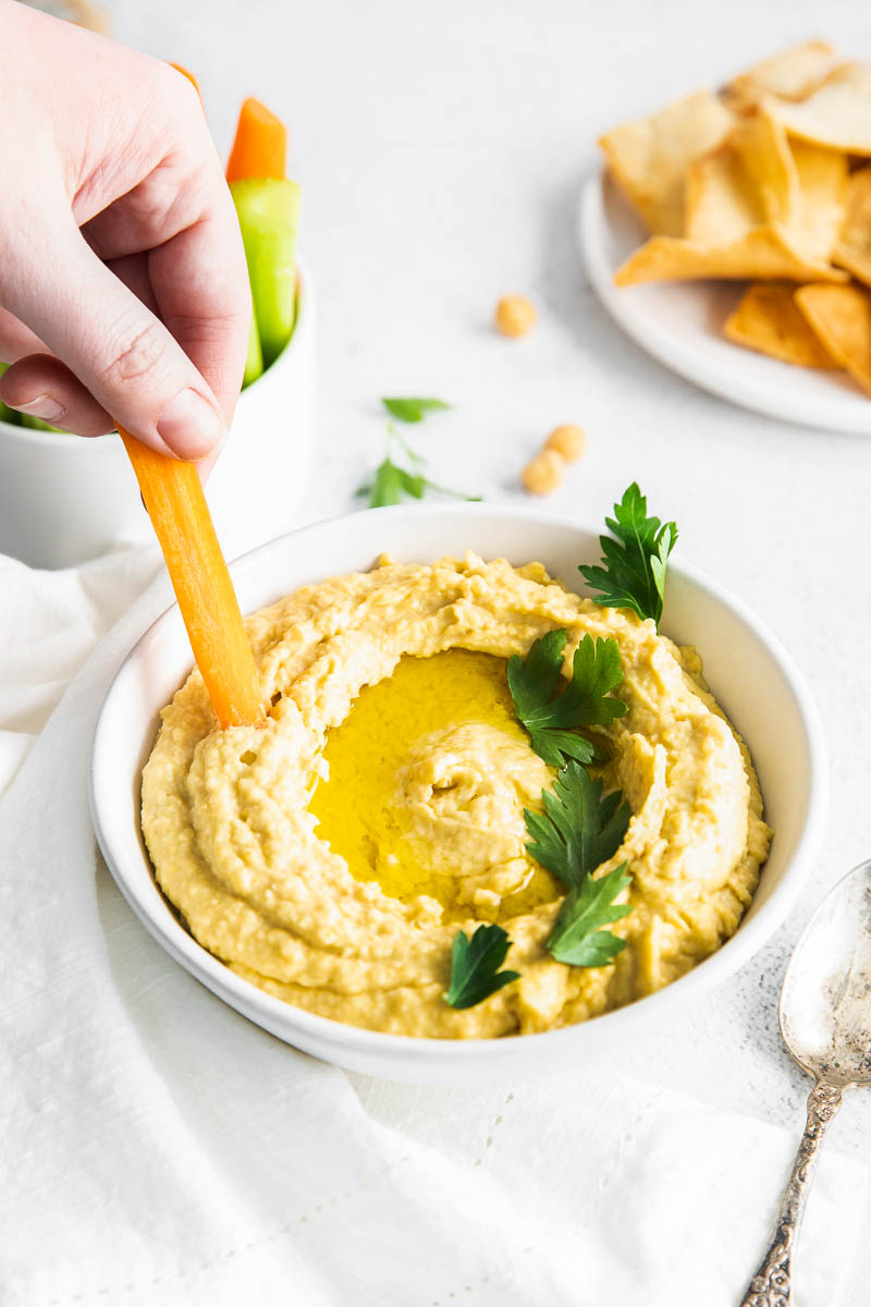 A carrot stick being dipped into a bowl full of hummus.