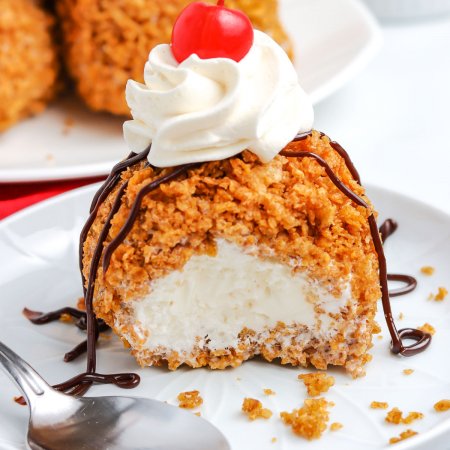 A close up picture of finished Fried Ice Cream on a white plate topped with whipped cream and hot fudge.