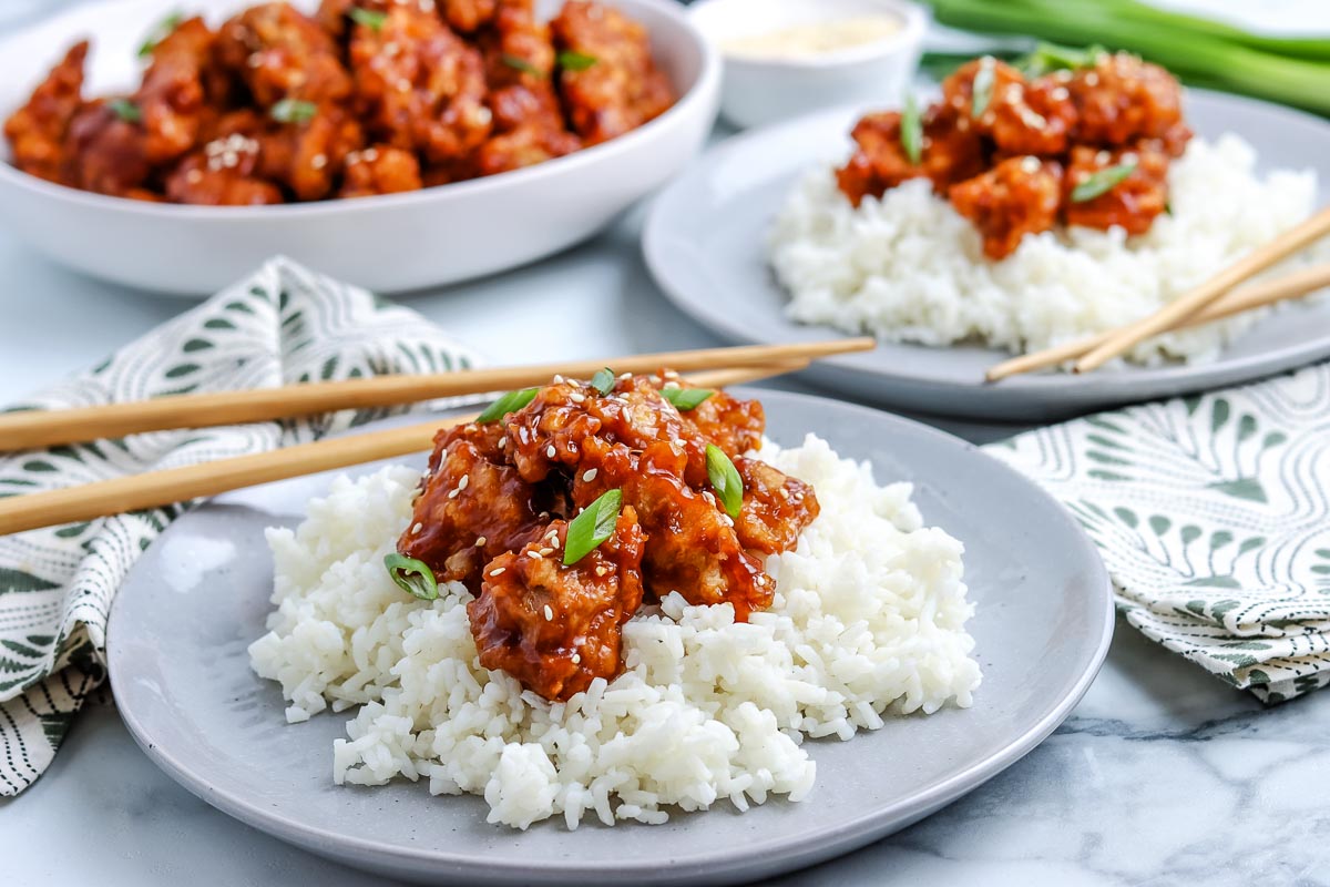 General Tso Chicken on top of white rice on a grey plate.