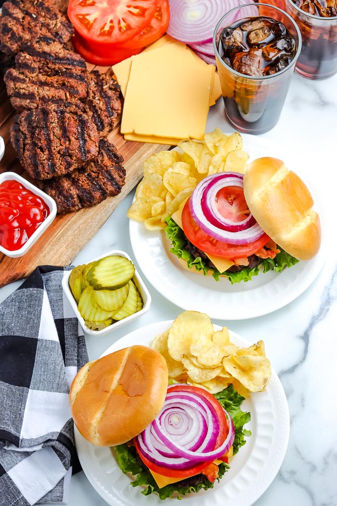 An overhead picture of grilled hamburgers on buns with lettuce, cheese, tomato, bacon, and onion.