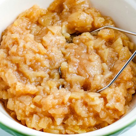A close up picture of chunky applesauce in a bowl with a potato masher.