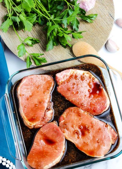 Four pork chops marinating in a baking dish.