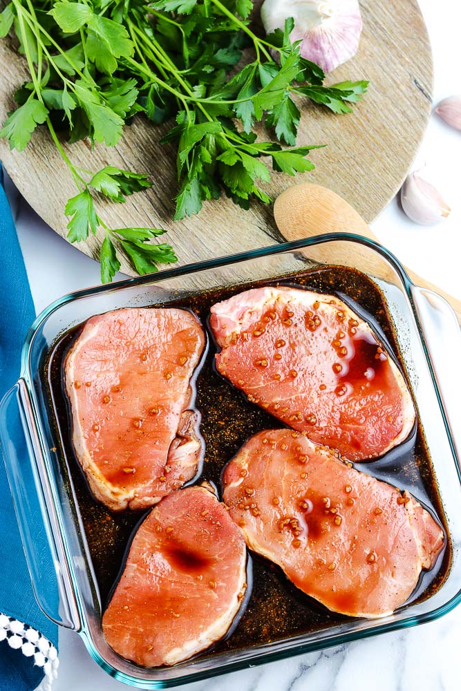 Four pork chops marinating in a baking dish.