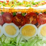 A close up picture of the finished seven layer salad in a clear glass serving bowl.