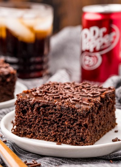 The finished Dr Pepper Cake slice on a white plate with a can of Dr Pepper in the background.