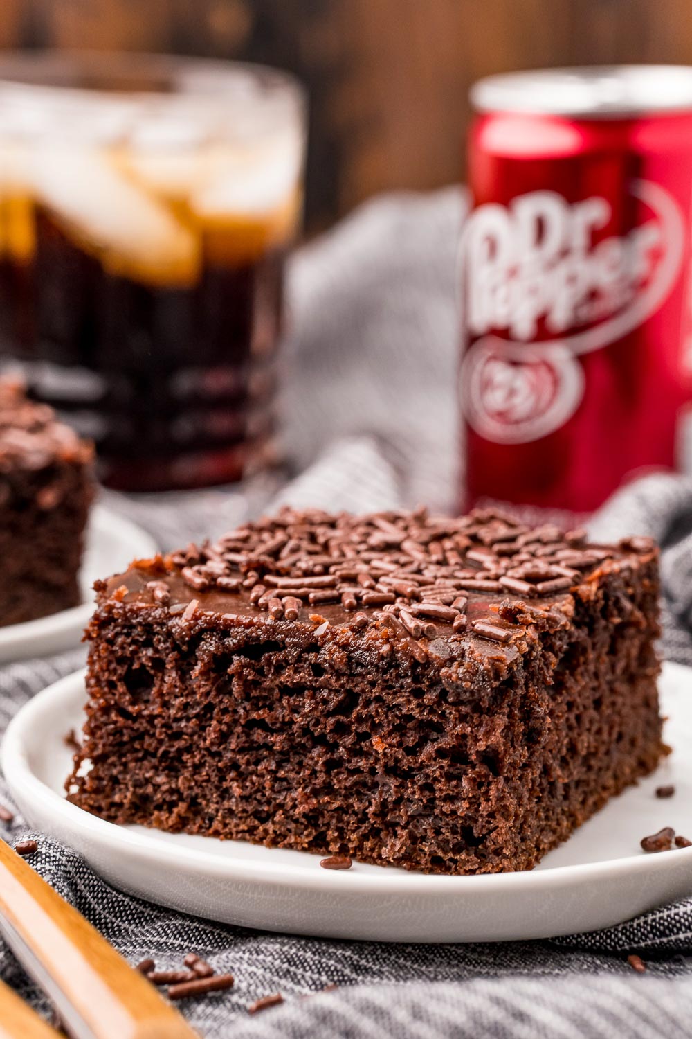 The finished Dr Pepper Cake slice on a white plate with a can of Dr Pepper in the background. 