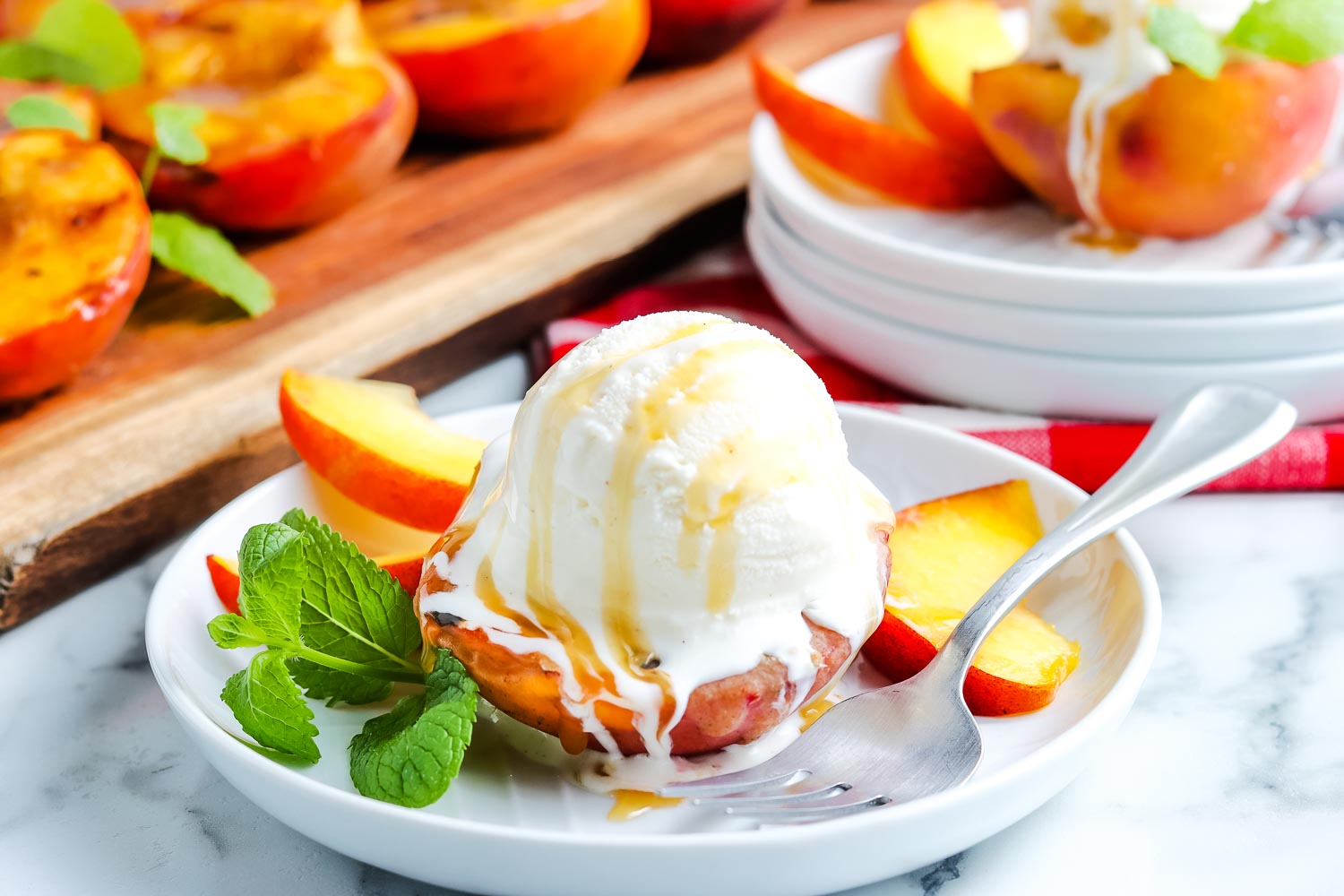 Grilled peaches with ice cream and caramel sauce on a white plate.