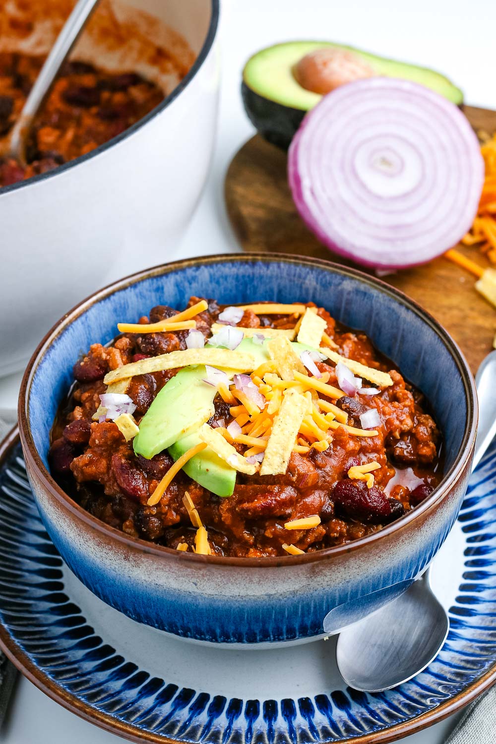 A bowl of Ground Turkey Chili with the white pot in the background. 