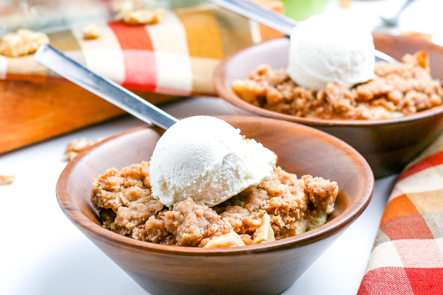Scoops of apple crisp in wooden bowls with a scoop of vanilla ice cream on top.