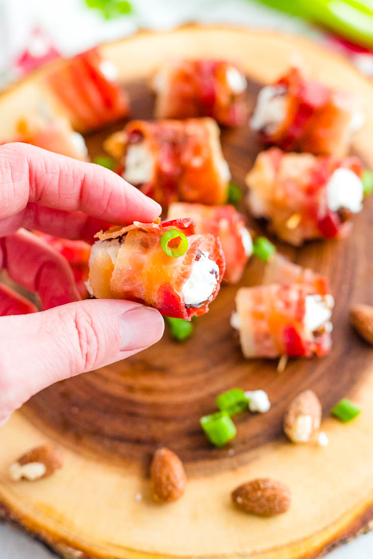 A hand picking up a bacon wrapped date stuffed with goat cheese.