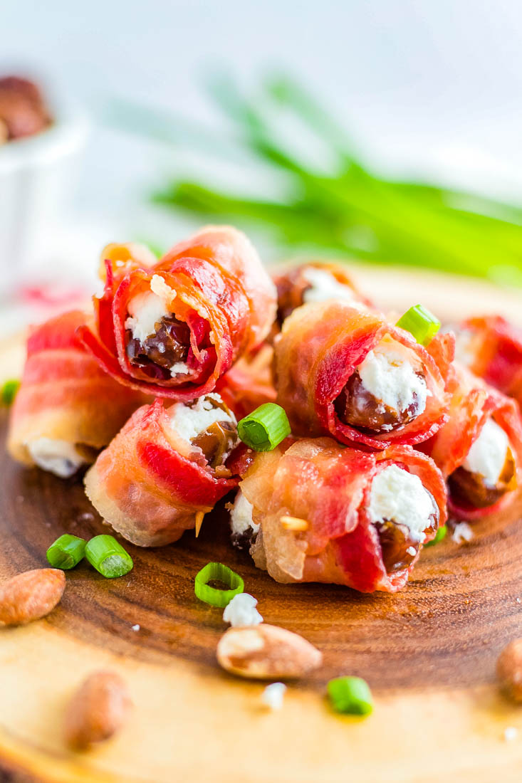 A pile of the finished Bacon Wrapped Dates on a widen cutting board.