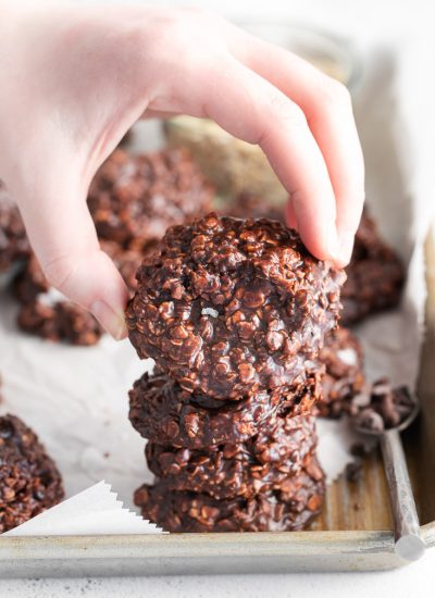 A stack of No-Bake Chocolate Oat Cookies and a hand picking up one of them.