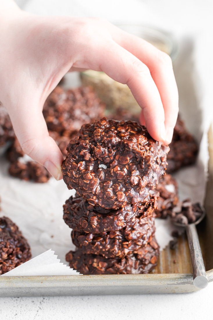 A stack of No-Bake Chocolate Oat Cookies and a hand picking up one of them. 