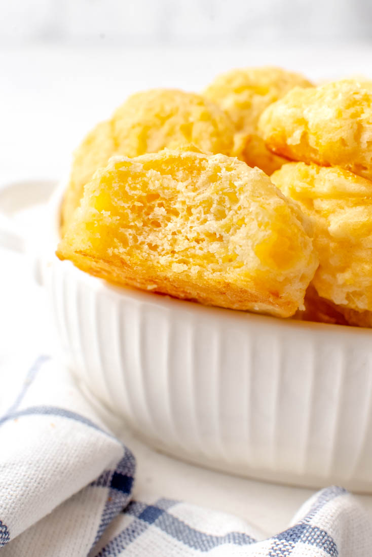 A bowl full of the finished Cheese Drop Biscuits with a bite taken out of one of the biscuits.
