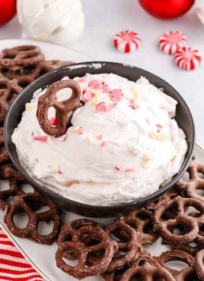 The finished Peppermint Cheesecake Dip in a black serving bowl with a chocolate covered pretzel dipped into it.