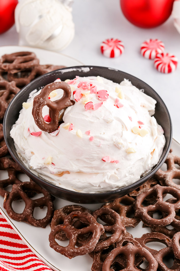 The finished Peppermint Cheesecake Dip in a black serving bowl with a chocolate covered pretzel dipped into it.