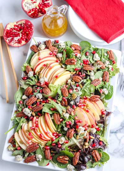 An overhead picture of the finished Pomegranate Salad on a white serving platter with the dressing in a bottle in the background.