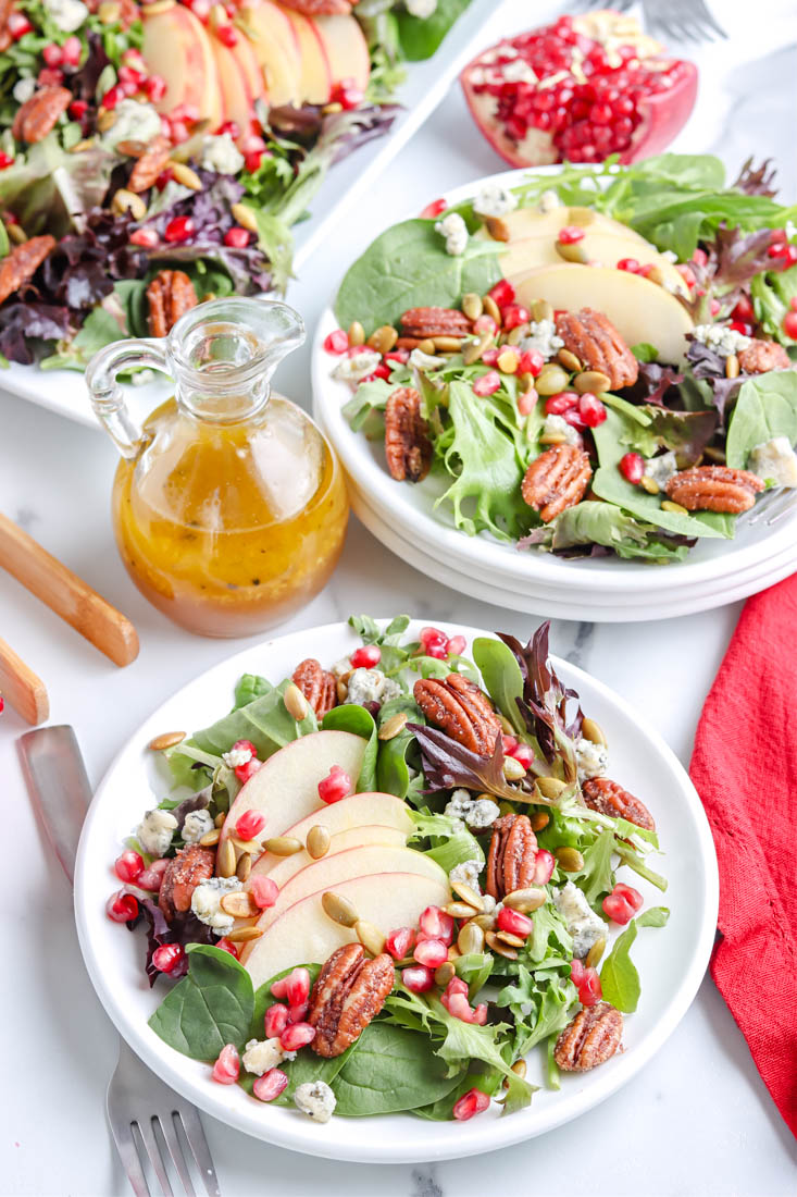 Pomegranate Salad on two white salt plates with a bottle of homemade dressing in the background.