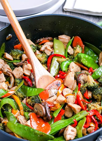 A wooden spoon scooping up some of the Chicken And Peppers Stir Fry.