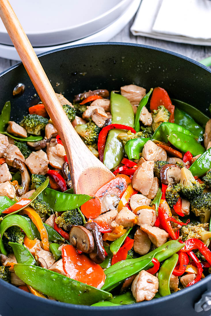 A wooden spoon scooping up some of the Chicken And Peppers Stir Fry. 