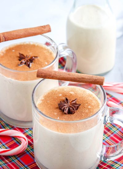 Homemade eggnog in a clear glass garnished with a cinnamon stick and star anise.