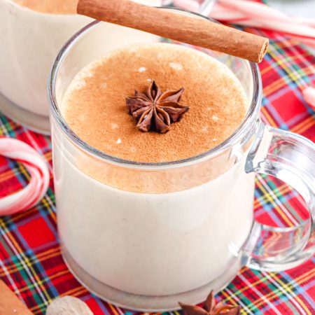 A close up picture of homemade eggnog in a clear glade garnished with ground cinnamon and a star anise.