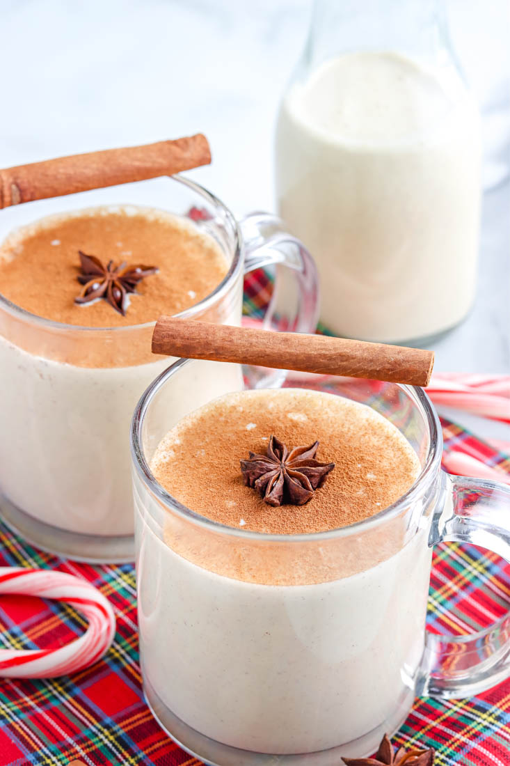 Homemade eggnog in a clear glass garnished with a cinnamon stick and star anise. 