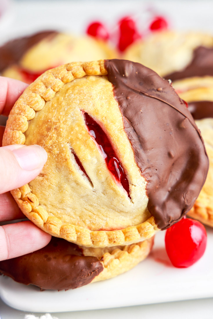 A hand holding up one of the finished Air Fryer Cherry Hand Pies.