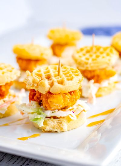 The finished Chicken and Waffle Sliders on a white serving platter drizzled with maple syrup.