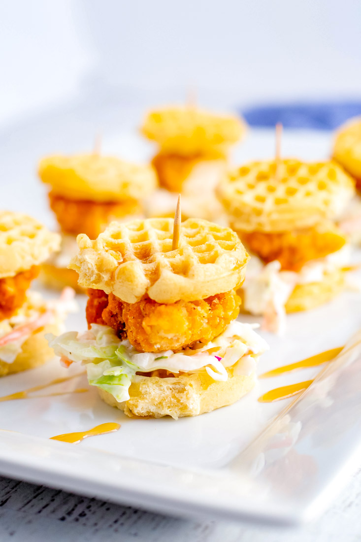 The finished Chicken and Waffle Sliders on a white serving platter drizzled with maple syrup.