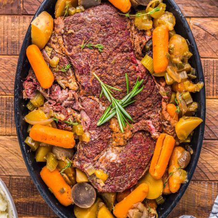 The finished Smoked Pot Roast on a black serving platter with carrots, celery, and potatoes.