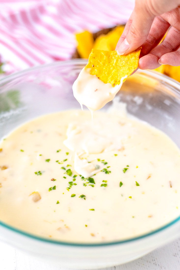 A chip dipping into a bowl full of Velveeta Queso Blanco Dip.