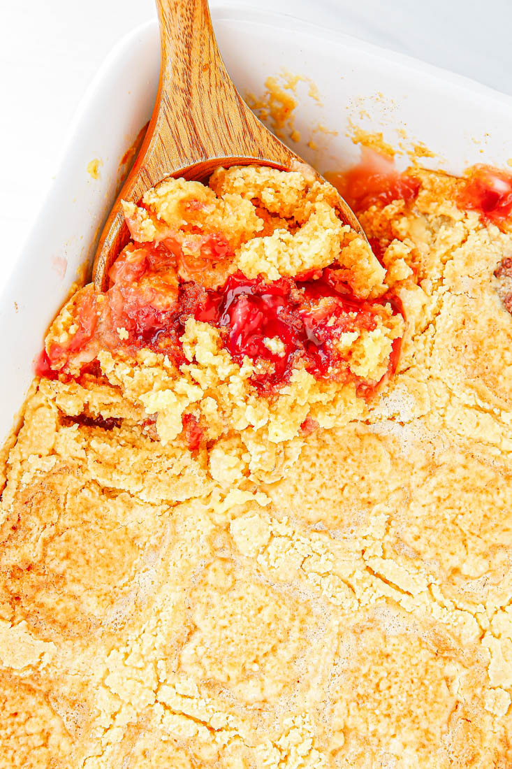 An overhead picture of the finished Cherry Pineapple Dump Cake with a serving spoon in the serving dish.