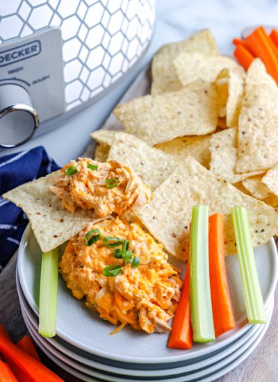 The finished Crockpot Buffalo Chicken Dip on a serving plate with chips, carrots, and celery.