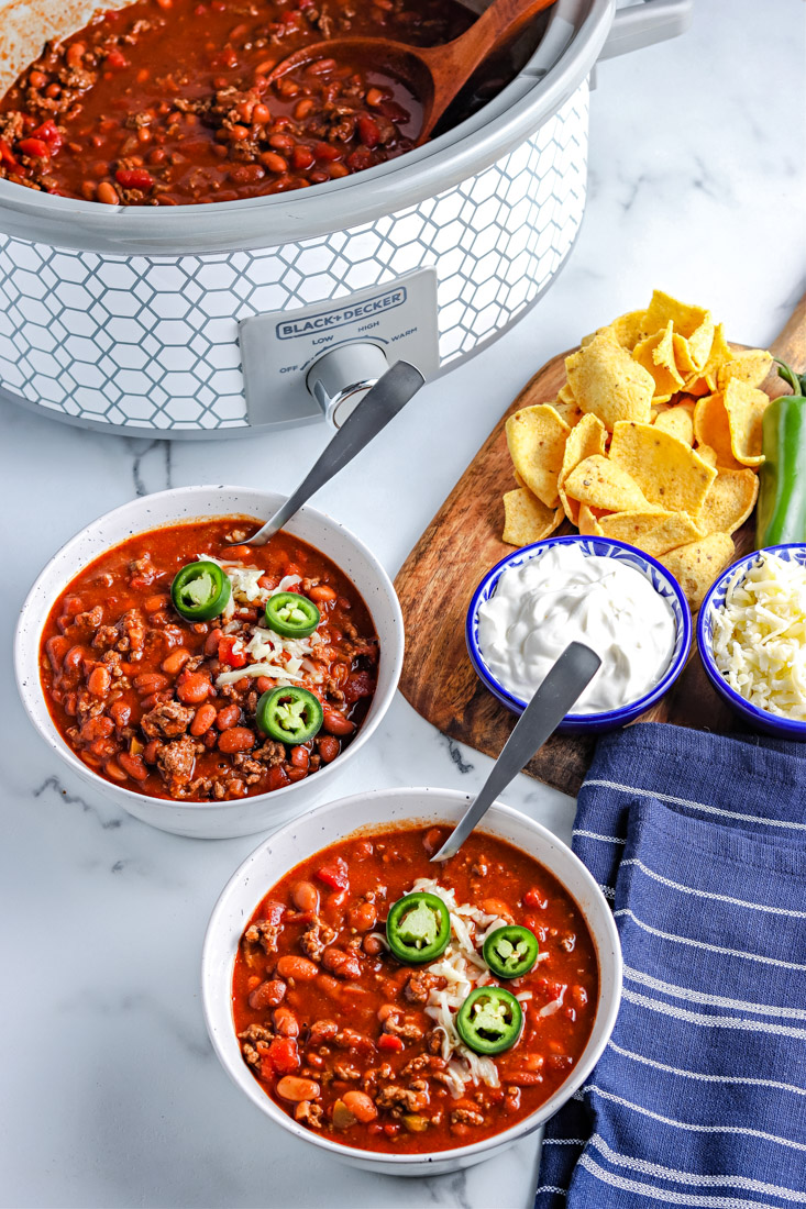 Two bowls of the crockpot chili and topping on the side.