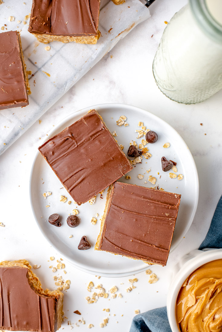 An overhead picture of two Chocolate Peanut Butter Bars on a white plate with a glass of milk.
