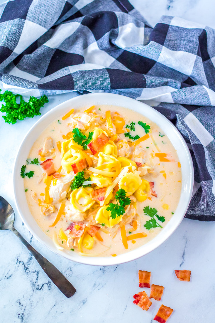 An overhead picture of a bowl full of Slow Cooker Creamy Tortellini Soup garnished with cheese and bacon. 