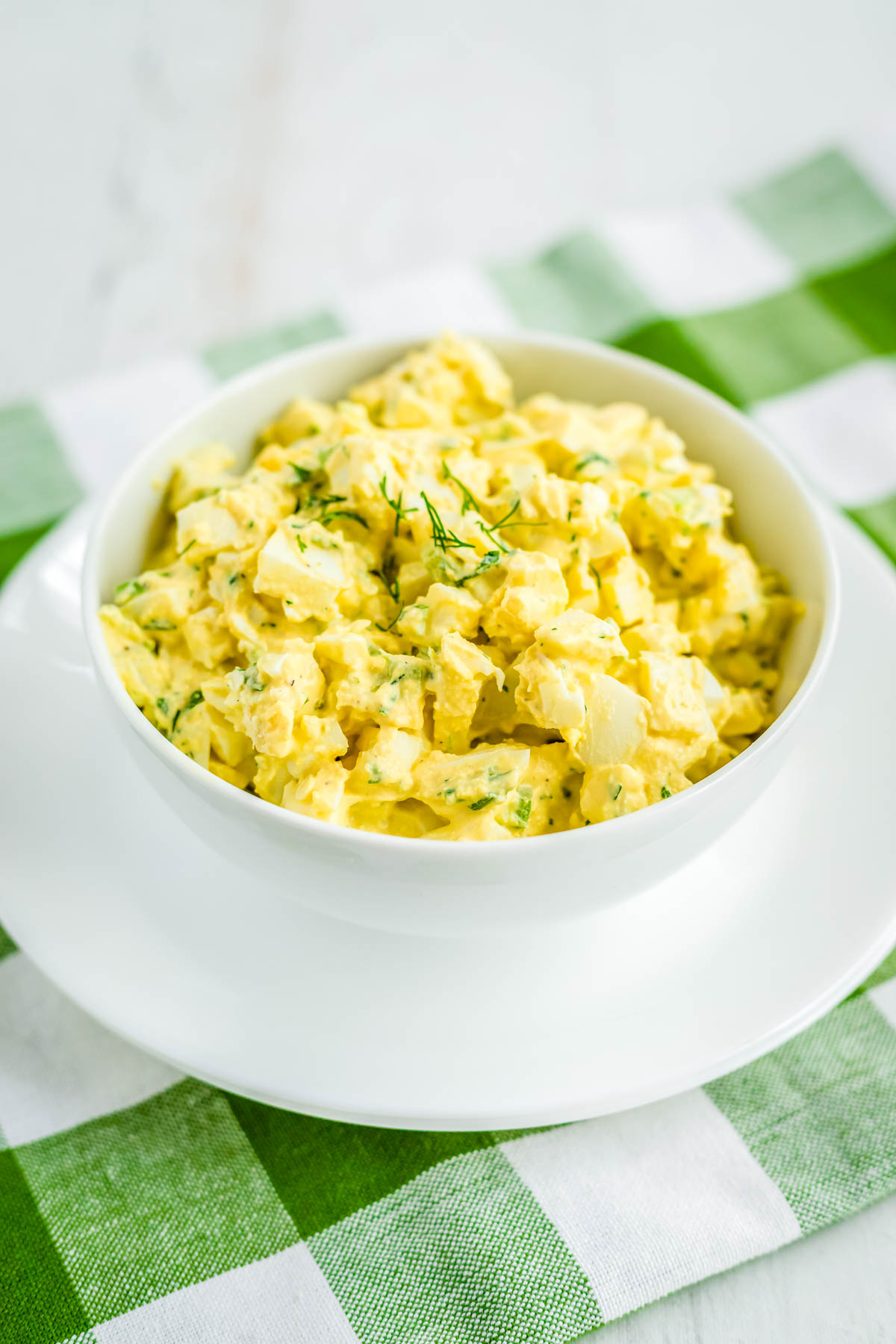 The finished egg salad in a white bowl garnished with dill.
