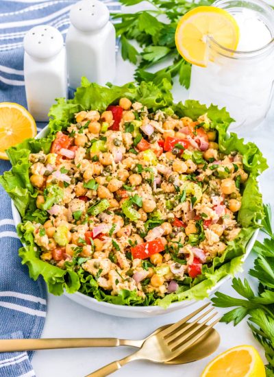 The finished Healthy Tuna Salad in a white serving bowl with cut lemons and salt and pepper nearby.
