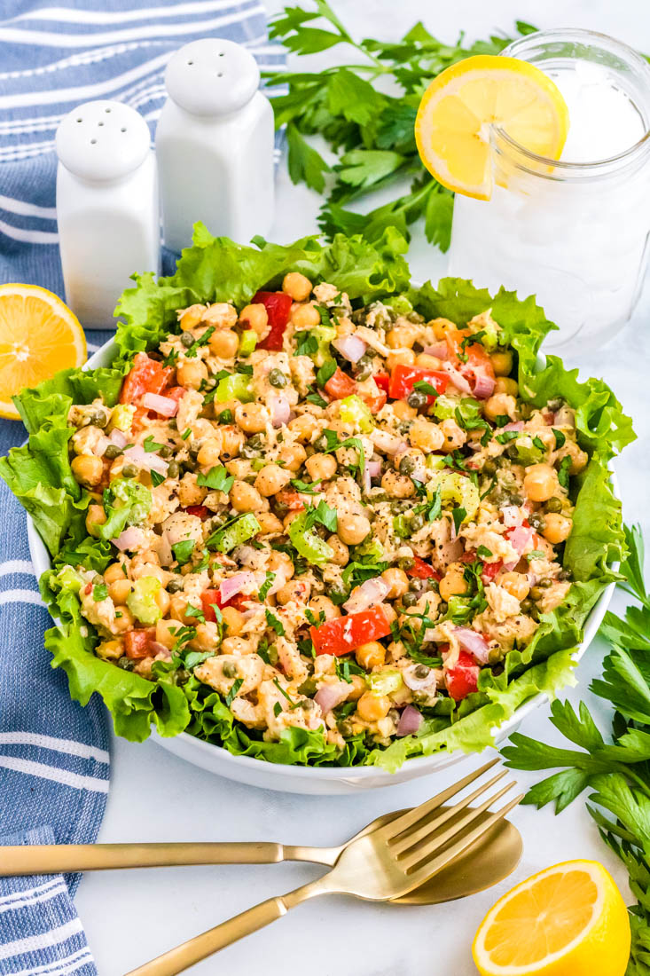 The finished Healthy Tuna Salad in a white serving bowl with cut lemons and salt and pepper nearby. 