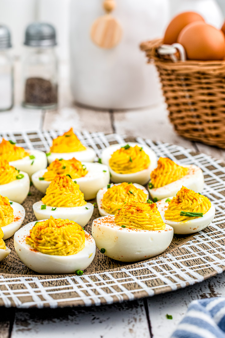 The finished Horseradish Deviled Eggs recipe on a wooden platter garnished with chives and paprika.