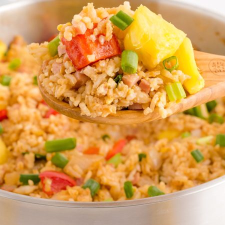 A wooden spoon picking up some pineapple fried rice from the frying pan.