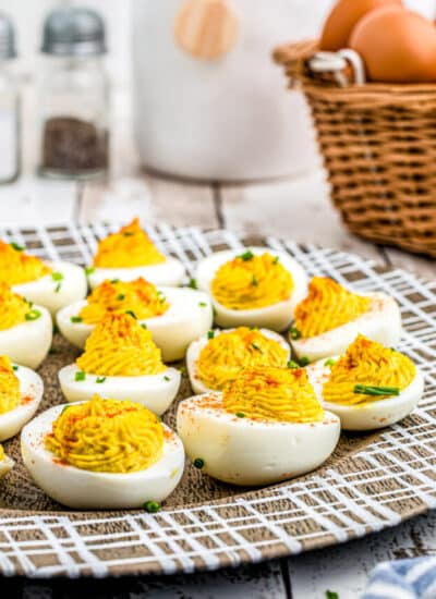The finished Horseradish Deviled Eggs recipe on a wooden platter garnished with chives and paprika.