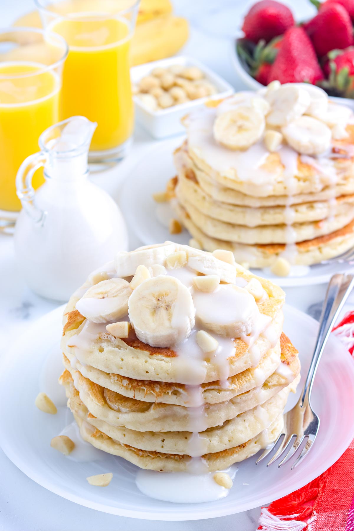 Two stacks of the finished Banana Pancakes on plates topped with sliced bananas, macadamia nuts, and coconut syrup.