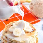 A close up picture of coconut pancake syrup being poured over banana pancakes.