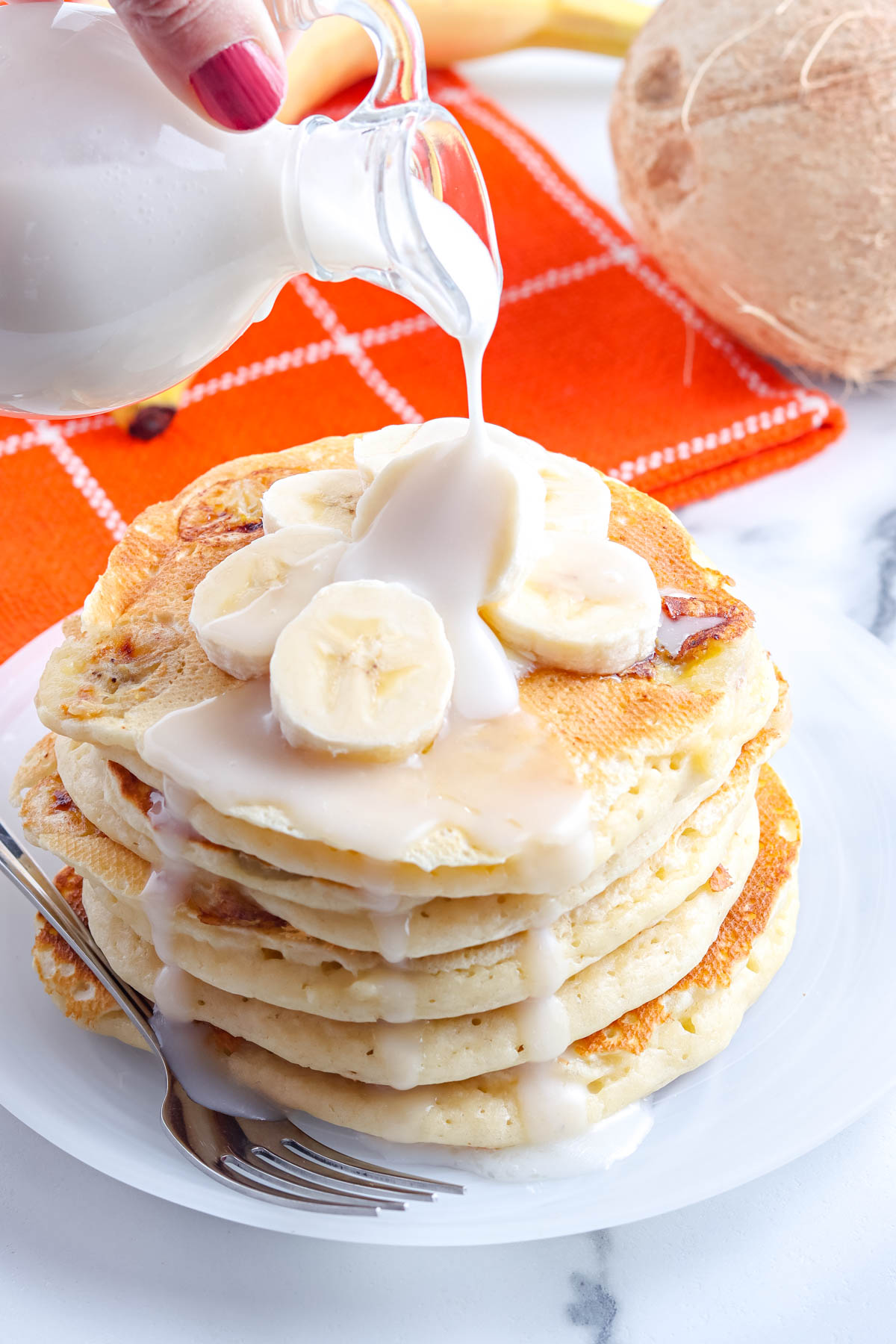 Hawaii-Style Coconut Syrup being poured over a stack of banana pancakes.
